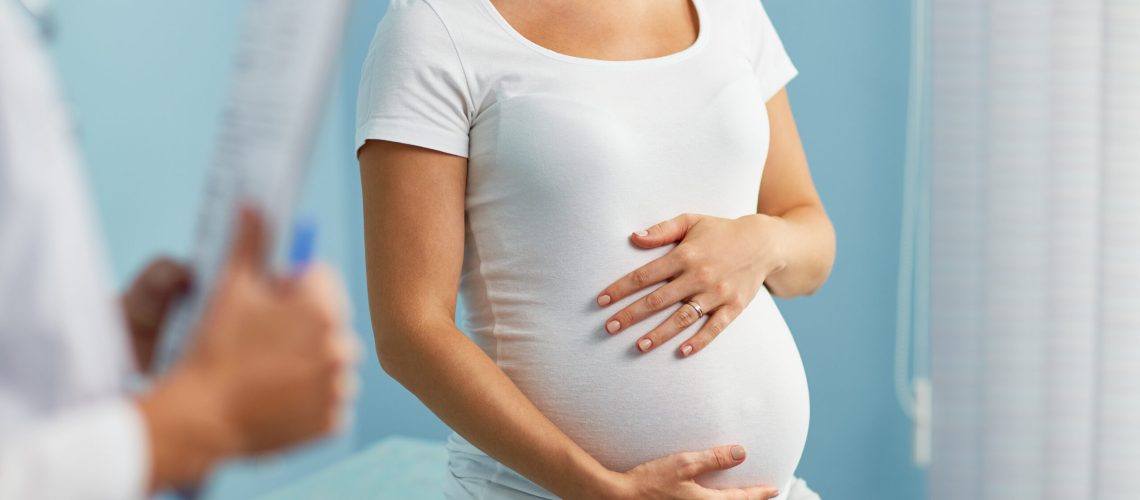 Pregnant woman with hands on stomach talking to obstetrician