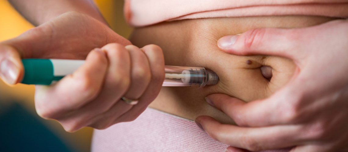 Woman making hormonal therapy injection into her belly. Close up syringe pen. Person in bedroom, in vitro fertilisation treatment.